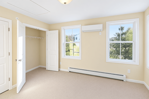 A room with a carpeted floor, a window with a view of trees, and a white door.