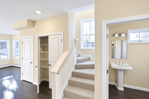 A white sink is in a white cabinet in a room with a staircase.
