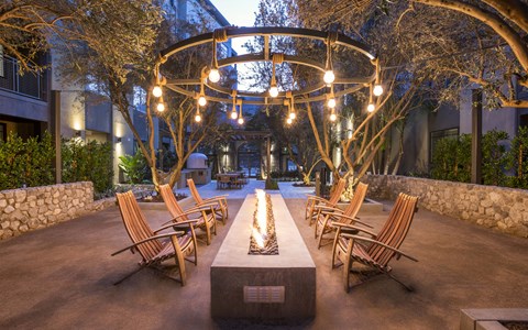 A beautifully lit outdoor seating area with wooden chairs and a fire pit.