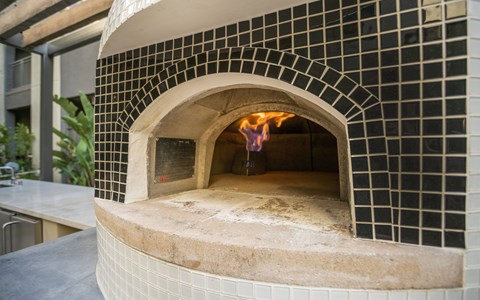 A brick oven with a fire inside is in the middle of a tiled wall.