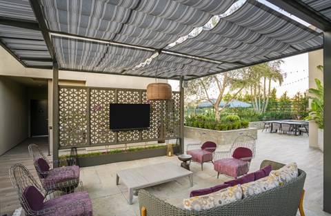 A patio with a grey sofa, chairs and a television.