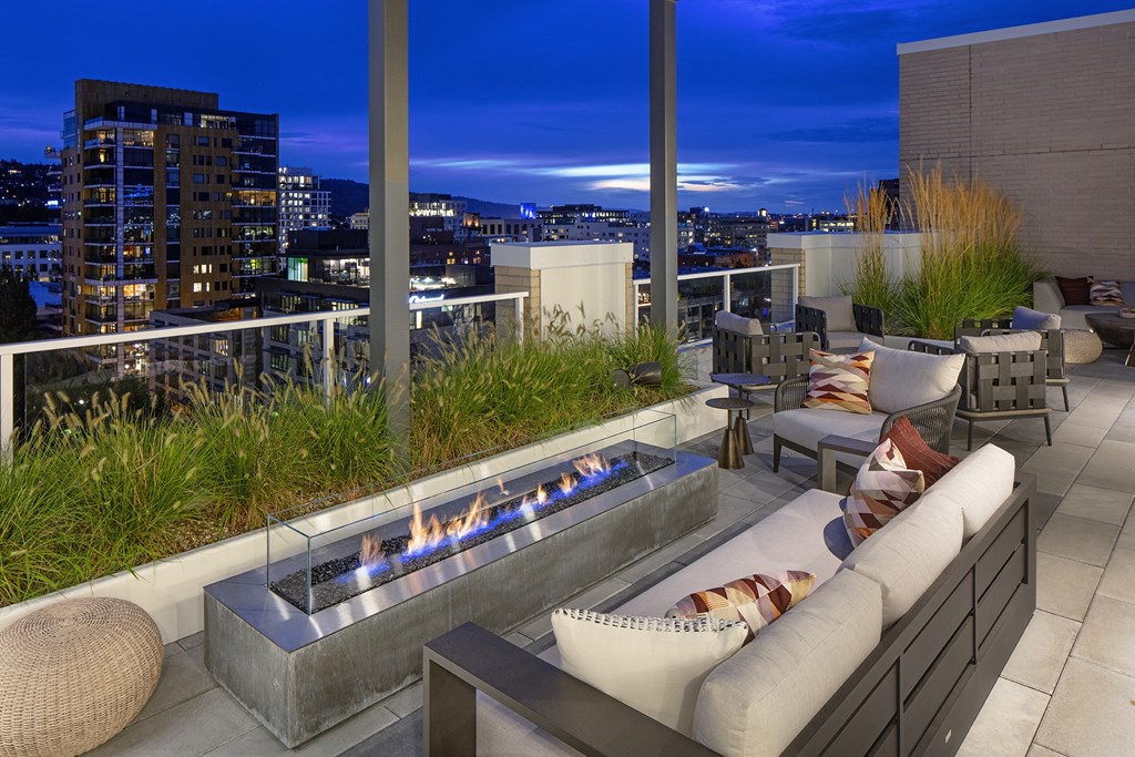 a rooftop terrace with couches and a fireplace overlooking a city at night