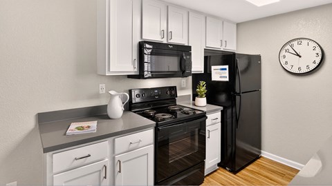 A black refrigerator sits in a kitchen with white cabinets and a black stove.