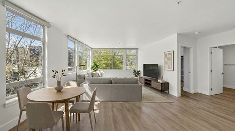 A living room with a grey couch, a wooden table and chairs, and a television.