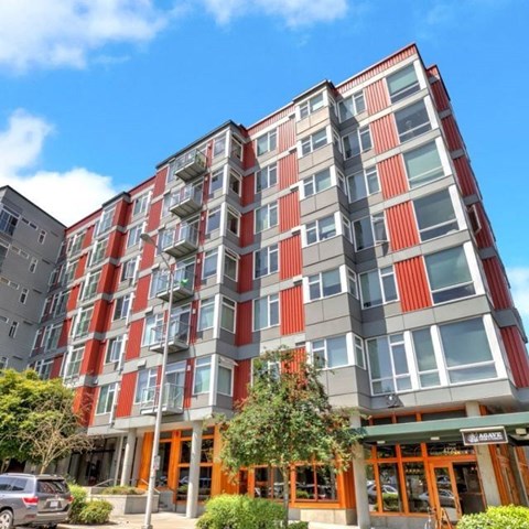 A modern multi-story building with red and grey exterior and a green awning.
