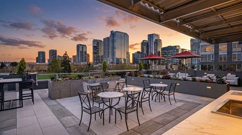 A rooftop patio with tables and chairs overlooking a city skyline at dusk.