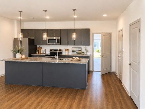 A modern kitchen with dark grey cabinets and a wooden floor.