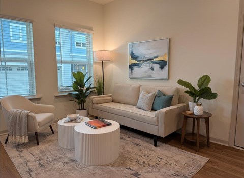 A living room with a beige couch, a chair, a table with a plant, and a painting on the wall. Calm Vibes