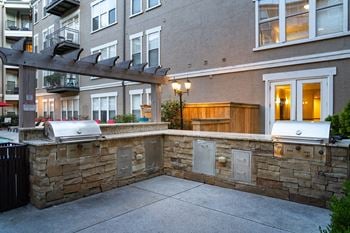 an outdoor kitchen with two bbq grills next to an apartment building