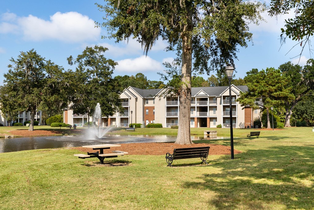 a park with a fountain and benches in front of an apartment building