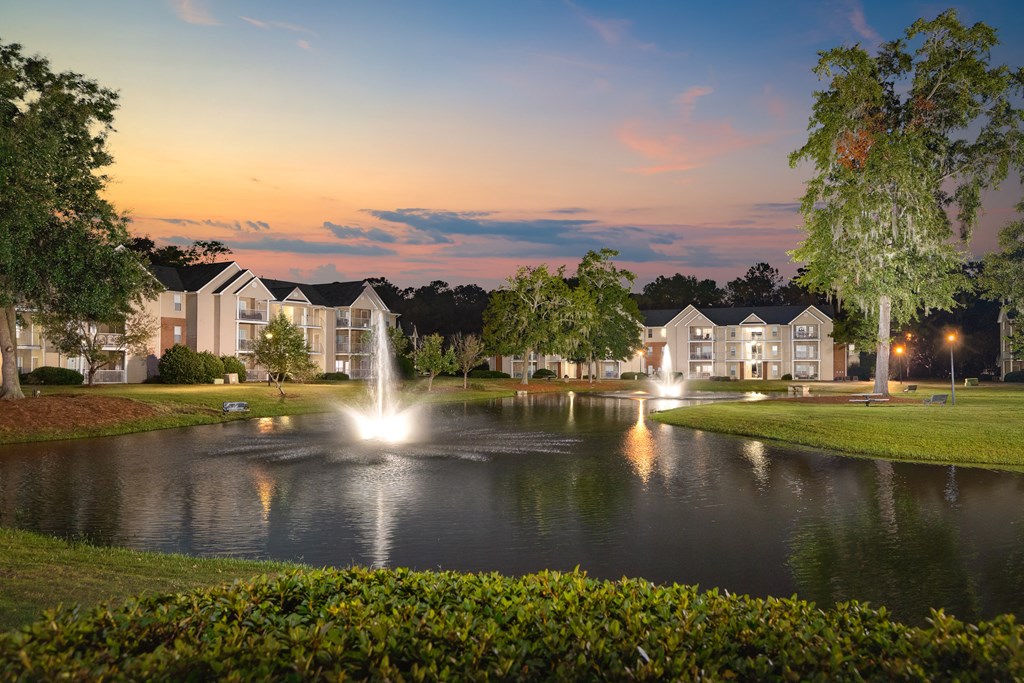 an evening view of a pond with a fountain in front of a building