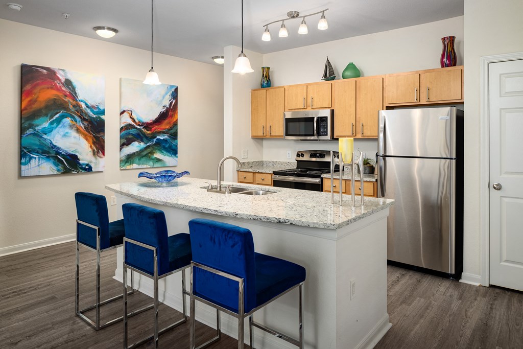 a kitchen with a large island with blue chairs and a stainless steel refrigerator