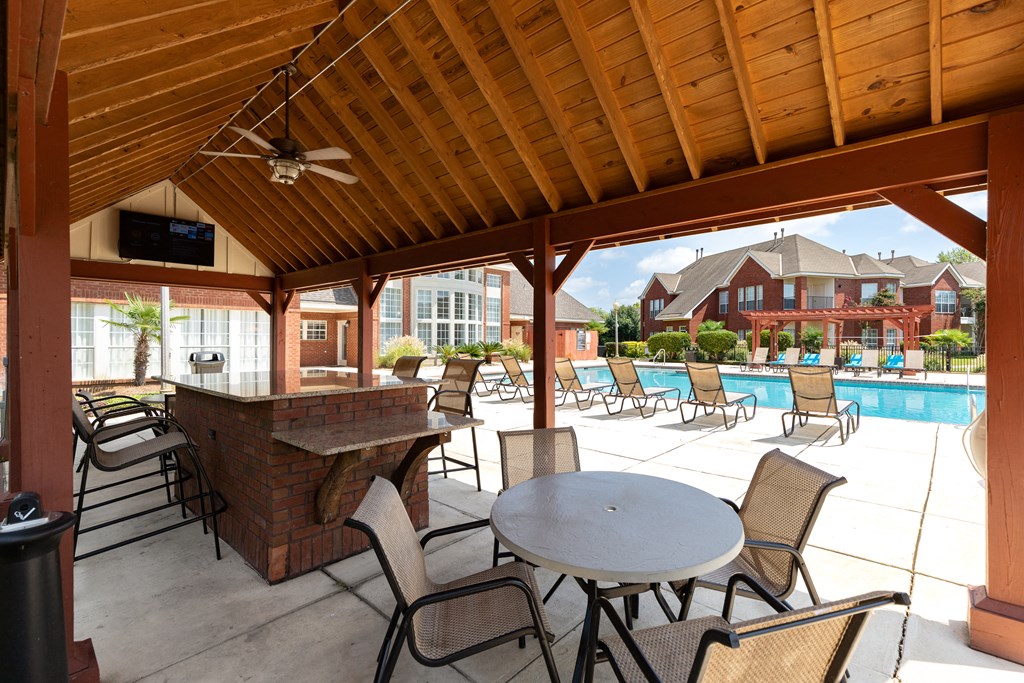 a covered patio with tables and chairs and a bar next to a pool