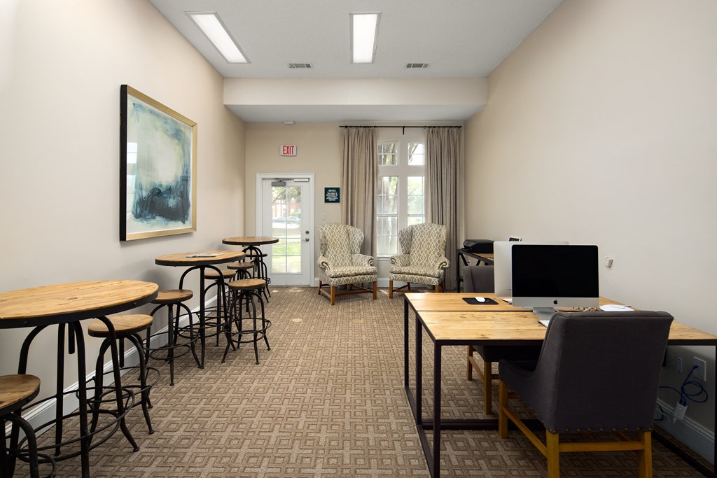 a common room with tables and chairs and a laptop computer on a desk