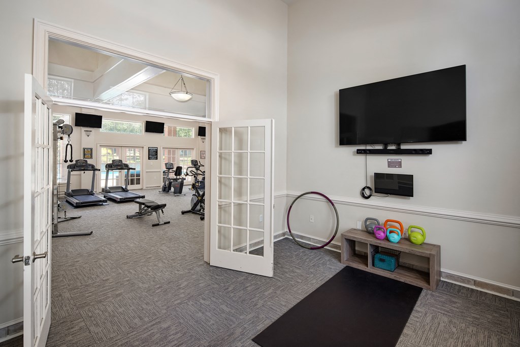 a gym with a flat screen tv and a doorway to a room with exercise equipment