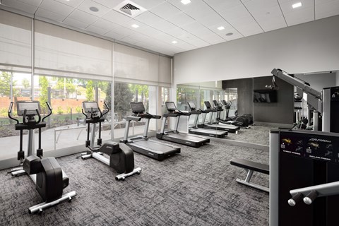 a row of treadmills and exercise machines in a room with large windows at Tower on Tenth Apartments, Birmingham