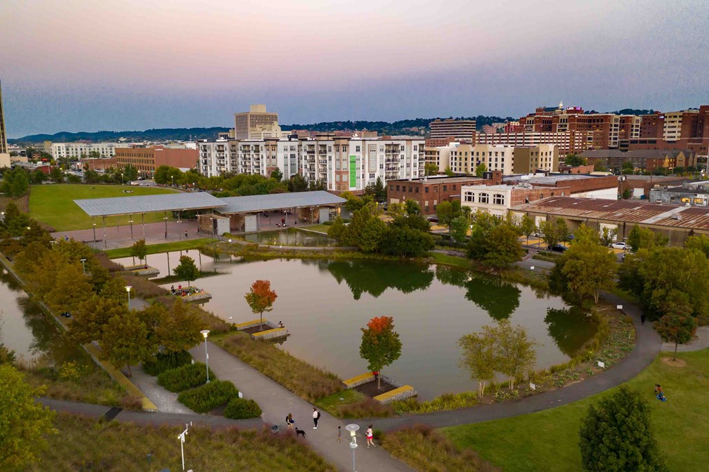 an aerial view of a park with a pond and city buildings
