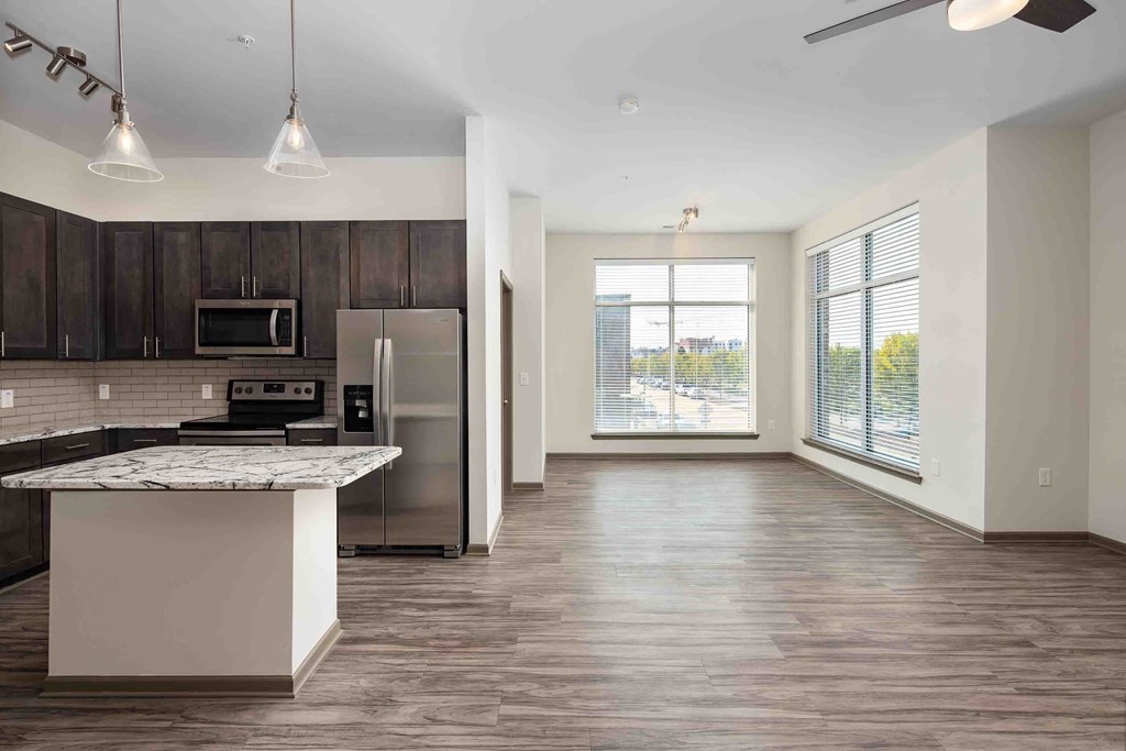 an empty living room with a kitchen and a large window