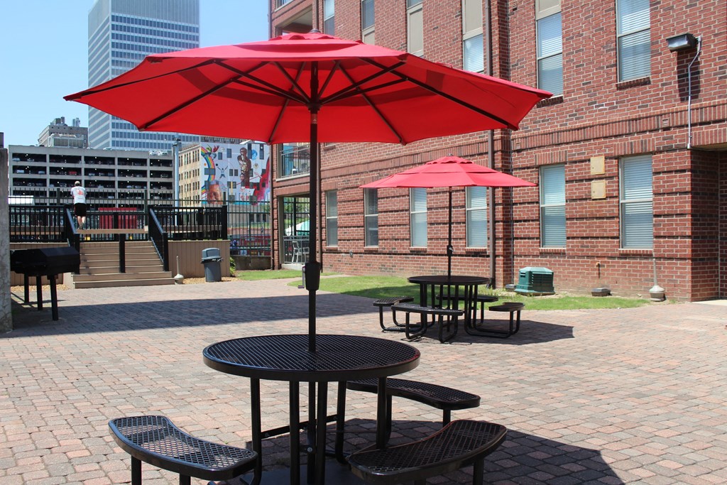 two tables with red umbrellas on a brick patio