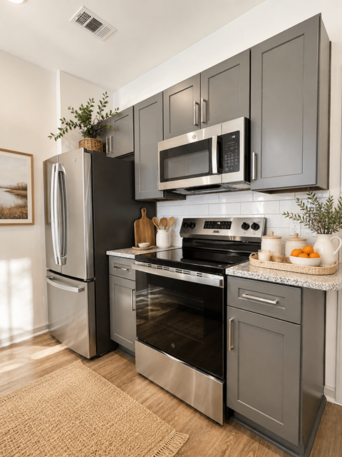 A modern kitchen with a stainless steel refrigerator, microwave, oven, and a cutting board on the counter.