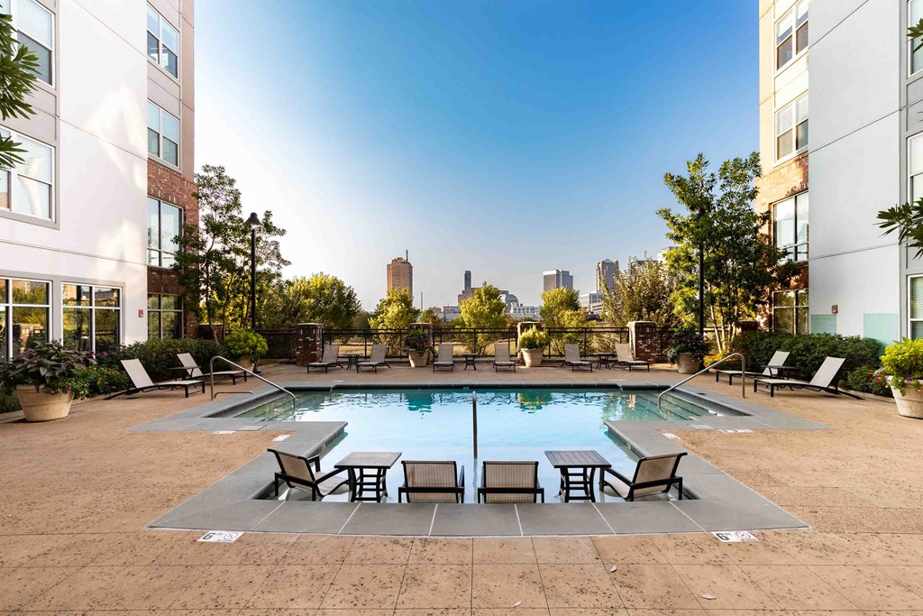 an outdoor pool with chairs and a city skyline in the background