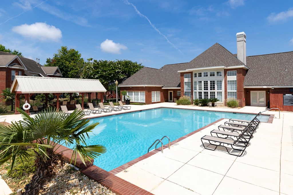 a swimming pool with lounge chairs in front of a house