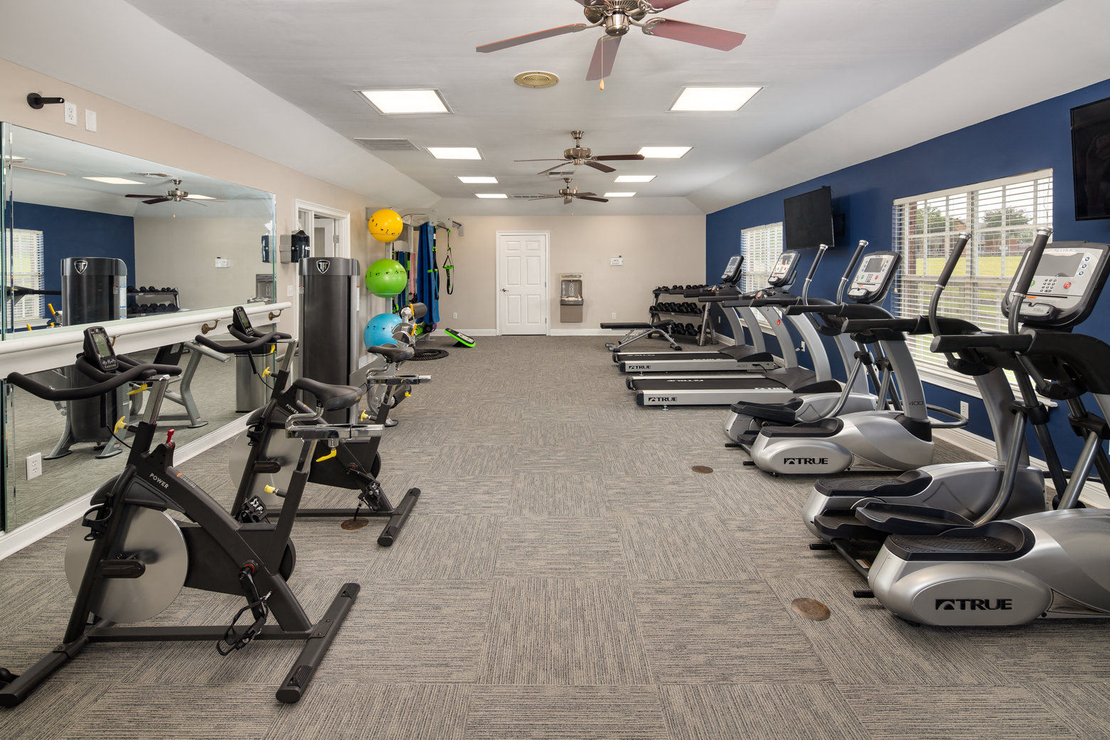 a gym with cardio exercise machines and a ceiling fan