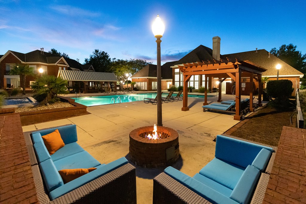 a swimming pool with blue chairs and a fire pit at night
