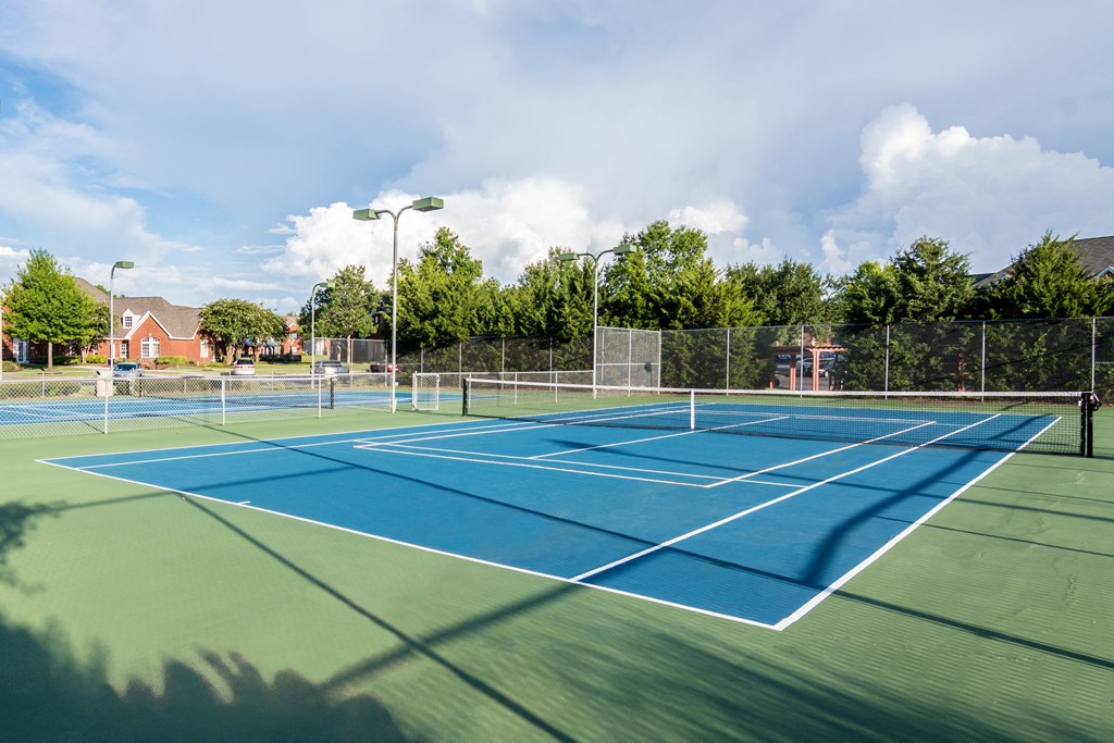 two tennis courts with trees and houses in the background