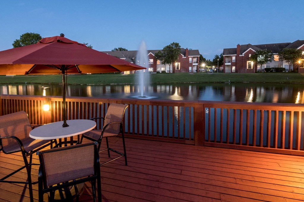 a deck with a table and chairs overlooking a lake and a fountain