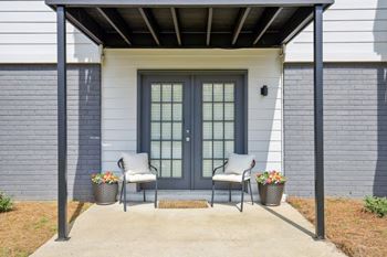 the front porch of a house with two chairs and a door