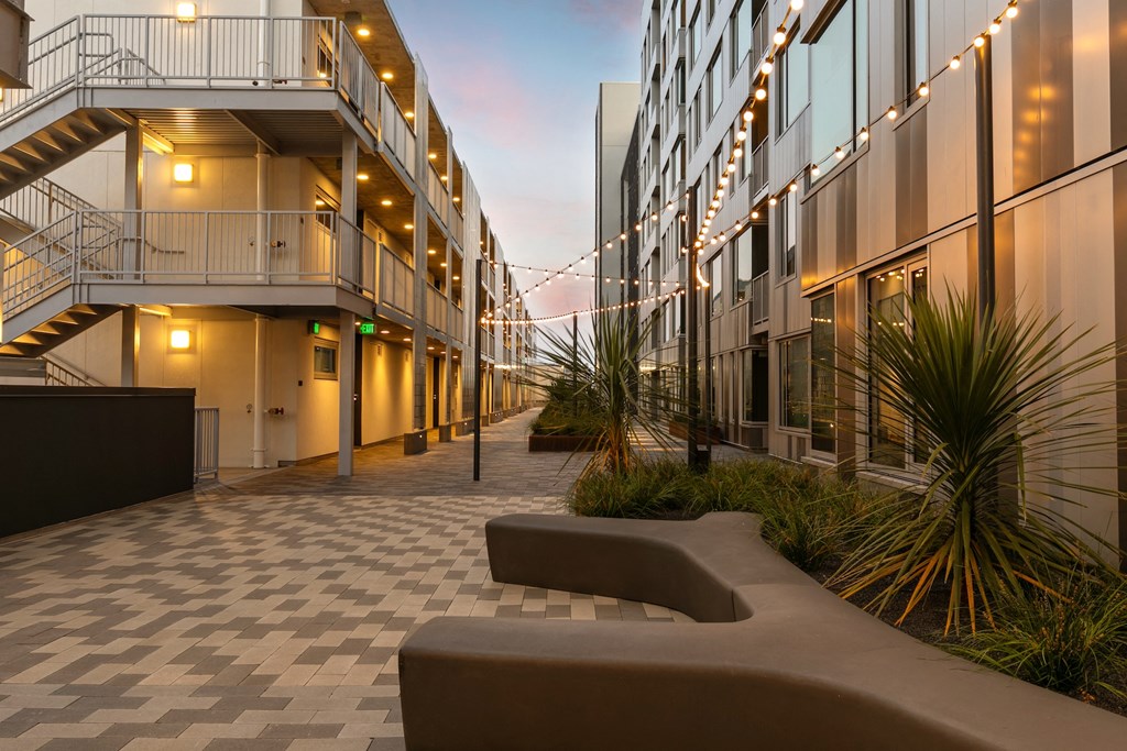 a courtyard with a bench and buildings with lights