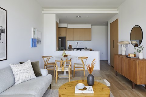 A modern living room with a grey couch, wooden chairs, and a coffee table with a book and vase on it.