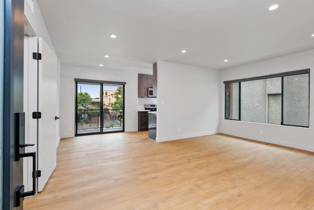 a living room with white walls and a sliding glass door to a kitchen