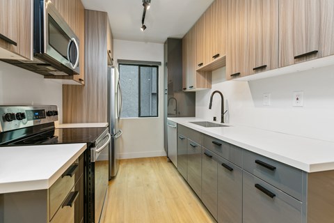 a kitchen with white counters and wooden cabinets and a stainless steel refrigerator