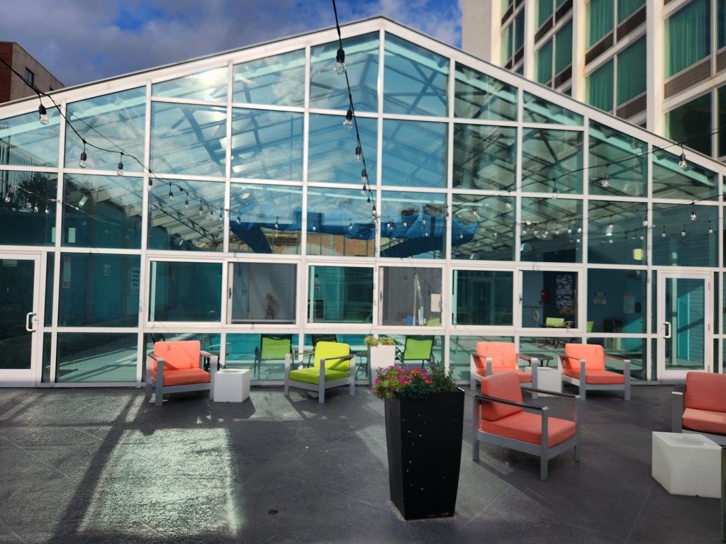 A glass building with orange chairs and a black planter in front.