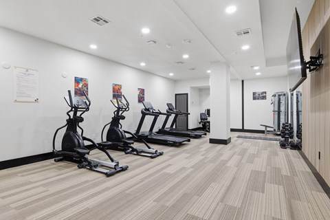 A gym with treadmills, elliptical machines, and a flat screen TV.