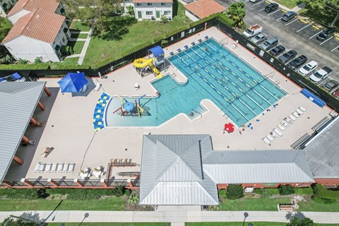 An aerial view of a swimming pool surrounded by a parking lot and buildings.