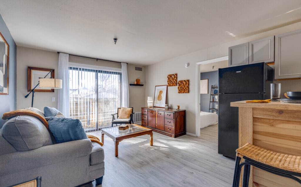 a living room with a couch and a table and a refrigerator at The Lodge Apartments, Tulsa Oklahoma