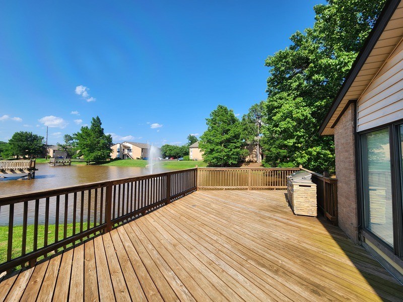 A wooden deck overlooks a body of water with a house and trees in the background.