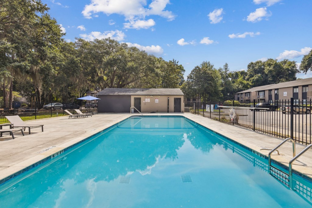 A swimming pool surrounded by trees and a building in the background.