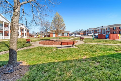 A park with a bench and a tree in the foreground and apartment buildings in the background.