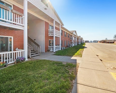 A row of red brick apartment buildings with white railings and steps leading to the doors.