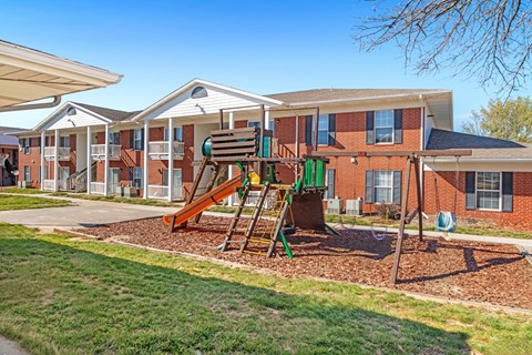 A playground with a slide and a green swing set in front of apartment buildings.