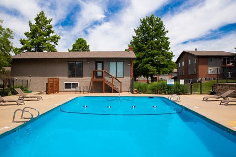 A swimming pool in front of a house with a deck and trees.