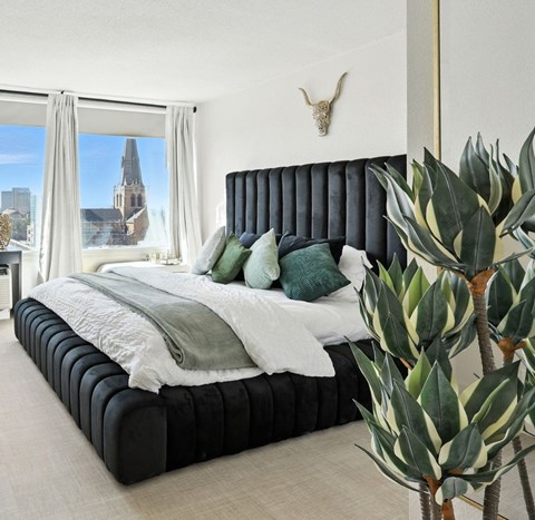 A bedroom with a large bed and a view of a city skyline through the window.