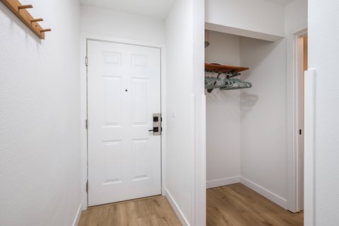A white door with a black handle is in a room with a white wall and a wooden floor.