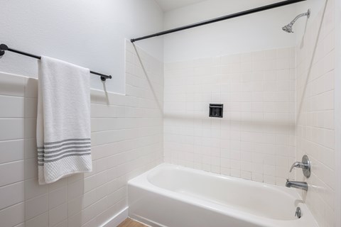 A white bathroom with a white tub and a white towel hanging on the rack.
