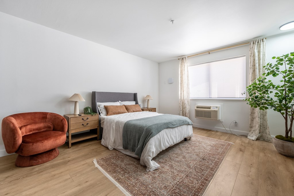 A bedroom with a bed, chair, and potted plant.