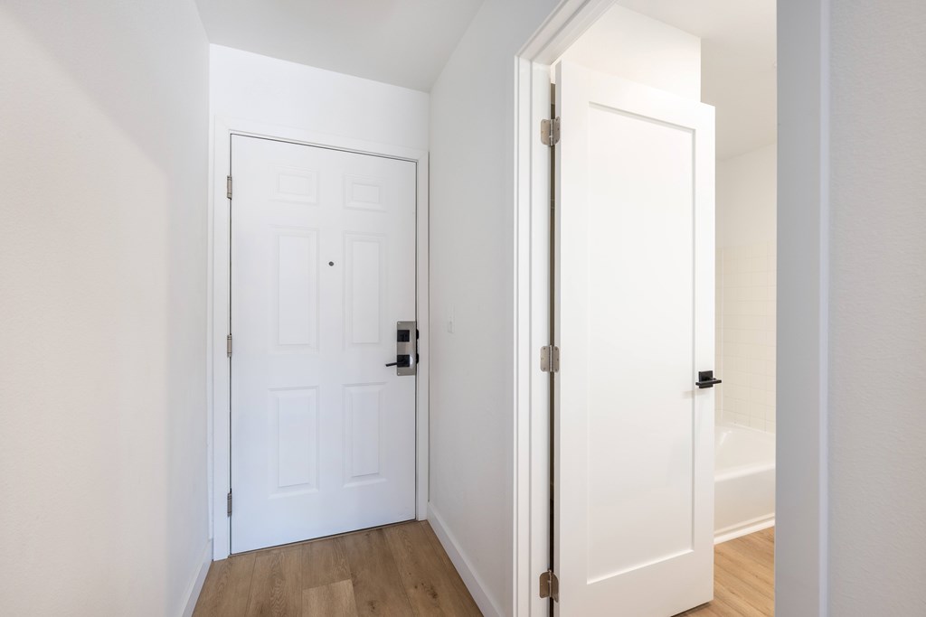 A white door with a black handle is open to a hallway.